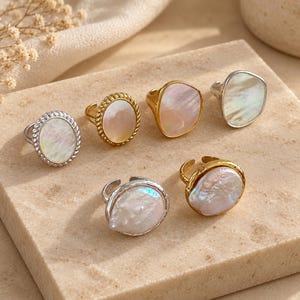 May include: A collection of six rings featuring iridescent mother-of-pearl inlays. The rings include various designs, such as smooth gold and silver bands, twisted rope-style borders, and irregular organic shapes with polished metallic finishes.