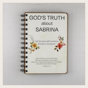 May include: A spiral-bound notebook with a cream-colored cover featuring the text GOD'S TRUTH about SABRINA, 30 Christian Affirmations Rooted in Scripture, and a Bible verse from Philippians 4:8, decorated with two floral illustrations in orange and yellow.
