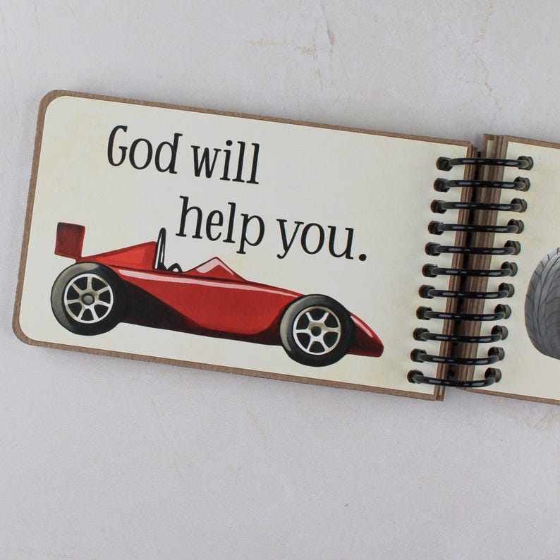 Peut inclure: Une page de livre &agrave; reliure spirale pr&eacute;sentant une illustration de voiture de course rouge et le texte noir God will help you. La page a un fond cr&egrave;me et une reliure en spirale m&eacute;tallique noire sur le c&ocirc;t&eacute; droit, montrant une autre page.