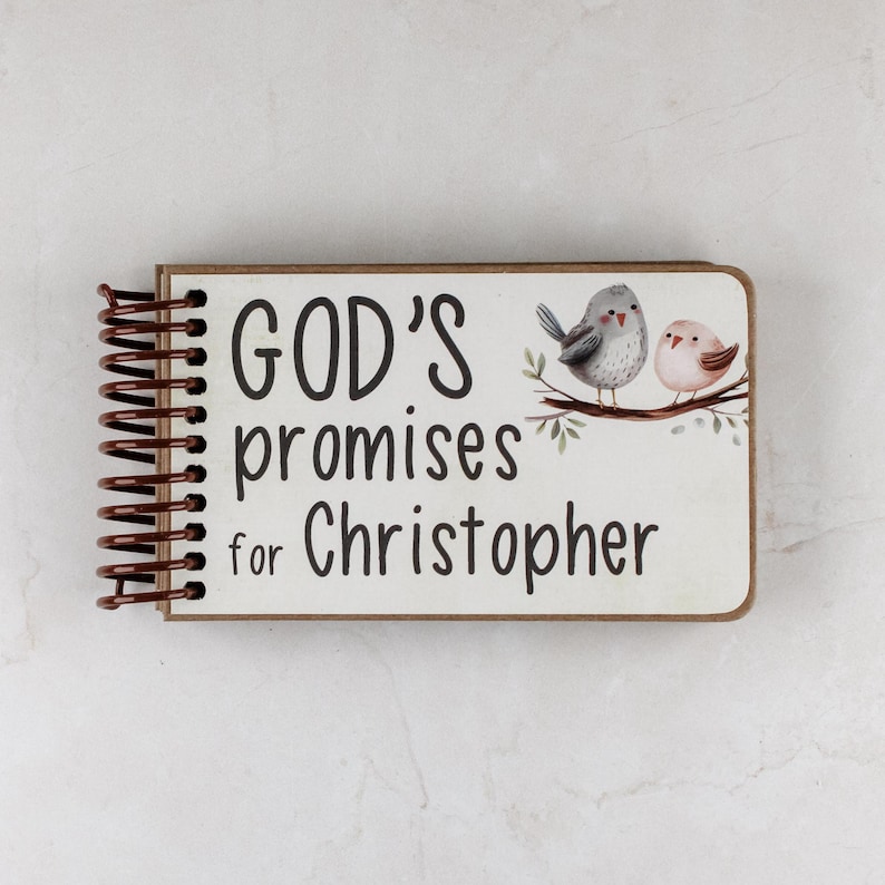 May include: A spiral-bound notebook with the text "GOD'S promises for Christopher." The cover features a watercolor illustration of two birds perched on a branch. The notebook has a brown wooden frame and a brown spiral binding.