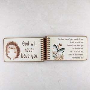 Puede incluir: Un libro de madera con encuadernaci&oacute;n en espiral que presenta un erizo de dibujos animados en la p&aacute;gina izquierda con el texto God will never leave you. La p&aacute;gina derecha muestra una ilustraci&oacute;n de mariposa y el texto The Lord himself.