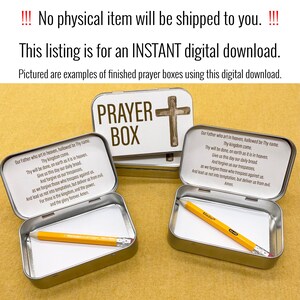 May include: Two silver metal boxes with a white background and the words "PRAYER BOX" printed in brown. The boxes are open and contain a white piece of paper and a yellow pencil. The boxes have a cross design on the lid.