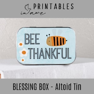 Może przedstawiać: Błękitno-biała metalowa puszka z ilustracją pszczoły i tekstem "Bee Thankful". Puszka jest pudełkiem na błogosławieństwa i ma rozmiar puszki Altoid.