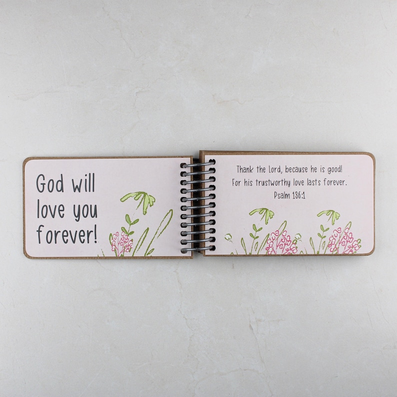 May include: Open spiral-bound journal with the text "God will love you forever!" on the left page. The right page reads "Thank the lord, because he is good! For his trustworthy love lasts forever. Psalm 136:1." Floral illustrations are present.