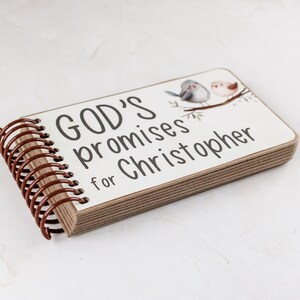 Puede incluir: Un cuaderno rectangular con encuadernaci&oacute;n en espiral y cubierta blanca que presenta el texto "GOD's promises for Christopher" en letras negras. La cubierta incluye una peque&ntilde;a ilustraci&oacute;n de dos p&aacute;jaros posados en una rama marr&oacute;n.