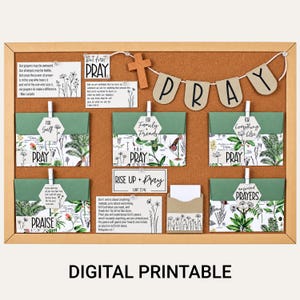 Op de afbeelding: Een kurken prikbord met een houten kruis, een banner met de tekst PRAY en diverse kaarten met botanische illustraties en teksten. De kaarten bevatten citaten en labels zoals For Self, For Family + Friends, For Everything Else en Answered Prayers.