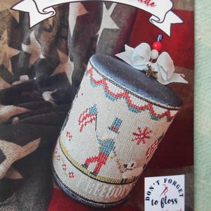 May include: A cylindrical needlepoint design featuring Uncle Sam's Parade. The design includes a figure in red, white, and blue, holding a flag. The text "Uncle Sam's Parade" is displayed above the design. The words "Don't forget to floss" are also visible.