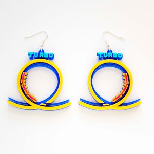 Pu&ograve; includere: Un paio di orecchini blu e gialli a forma di anello di montagne russe con la scritta "TURBO" in cima.