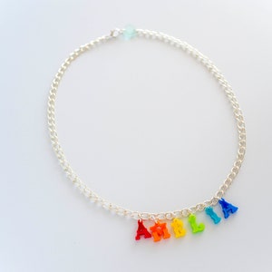Puede incluir: Un collar de cadena plateada con abalorios de letras de colores arco&iacute;ris que deletrean el nombre "Amelia".