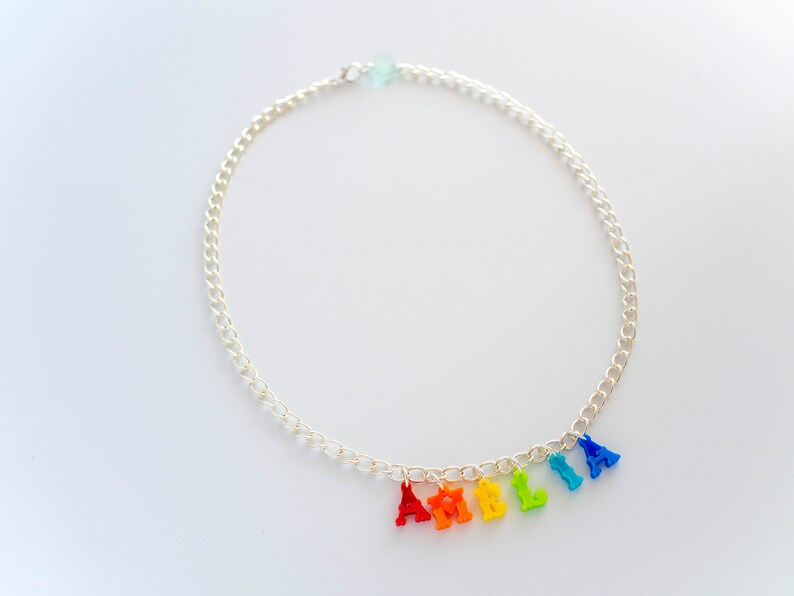 Puede incluir: Un collar de cadena plateada con abalorios de letras de colores arco&iacute;ris que deletrean el nombre "Amelia".