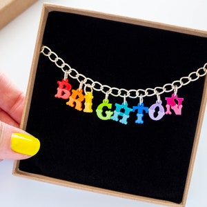 Puede incluir: Un collar de cadena de plata con abalorios de letras de colores que deletrean la palabra "BRIGHTON". Los abalorios son de colores arco&iacute;ris.