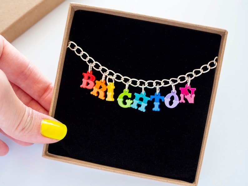 Puede incluir: Un collar de cadena de plata con abalorios de letras de colores que deletrean la palabra "BRIGHTON". Los abalorios son de colores arco&iacute;ris.
