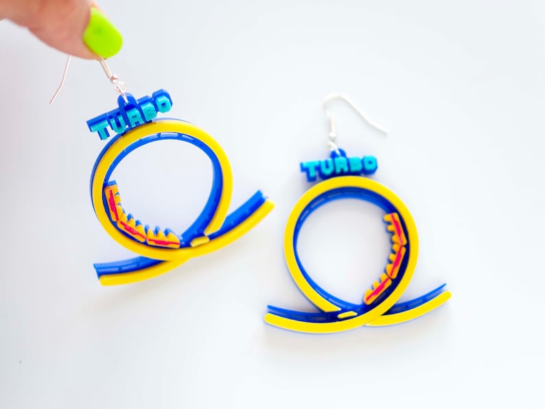 Pu&ograve; includere: Un paio di orecchini blu, gialli e rossi a forma di pista di montagne russe con la parola "TURBO" in cima.