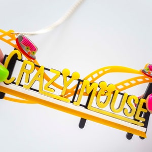 May include: A yellow and black necklace with a roller coaster design and the words "Crazy Mouse". The roller coaster has two pink and red cars.