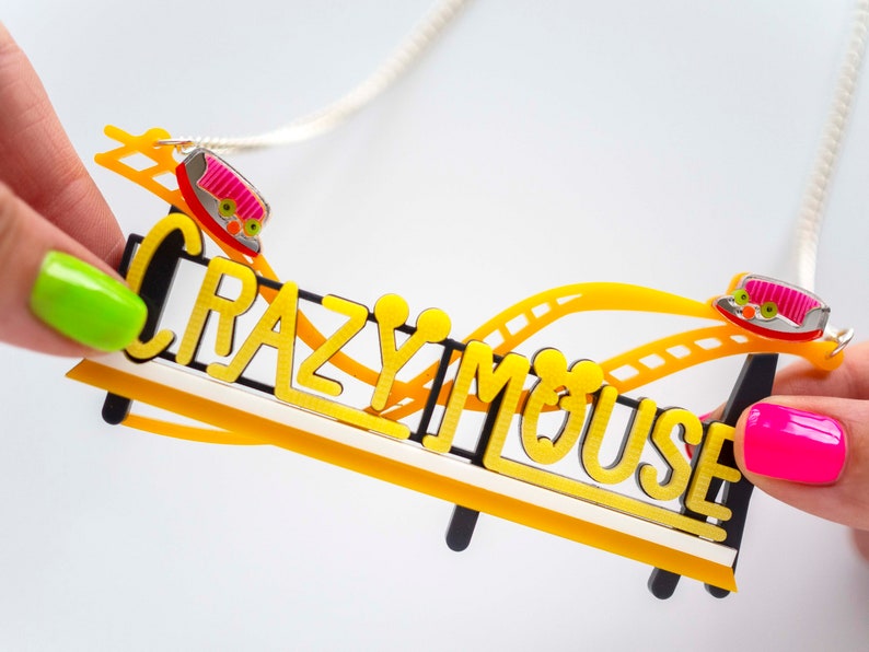 May include: A yellow and black necklace with a roller coaster design and the words "Crazy Mouse". The roller coaster has two pink and red cars.