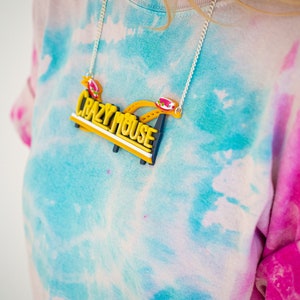 May include: A yellow and black necklace with the words "Crazy Mouse" on it. The necklace is worn by a person wearing a tie-dye shirt.