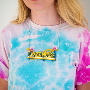 May include: A silver chain necklace with a yellow and blue "Crazy Mouse" sign pendant. The sign features a red and white roller coaster car.