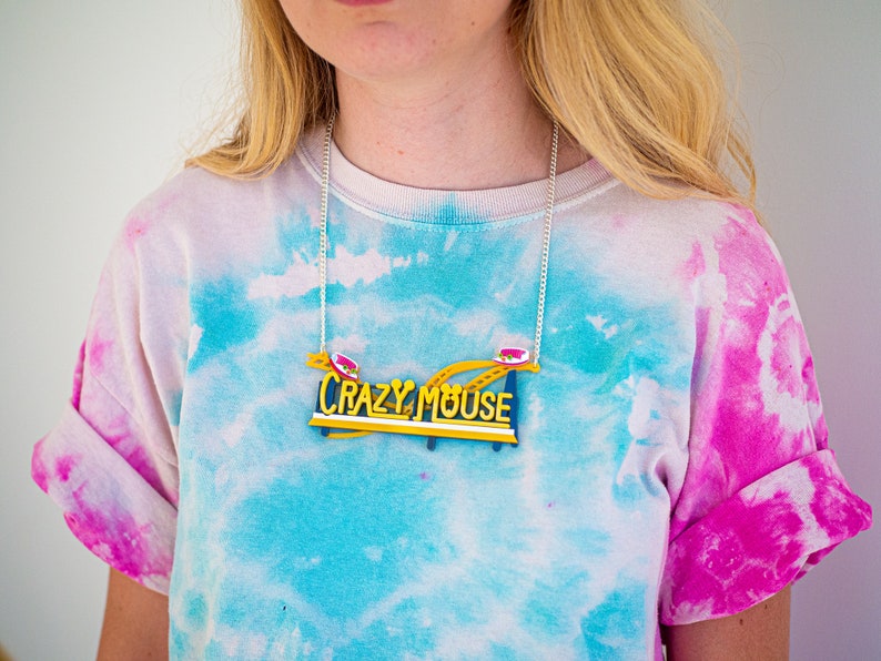 May include: A silver chain necklace with a yellow and blue "Crazy Mouse" sign pendant. The sign features a red and white roller coaster car.