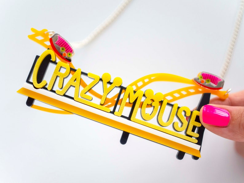 May include: A yellow and black necklace with a roller coaster design and the words "Crazy Mouse". The roller coaster has two small pink and yellow cars.