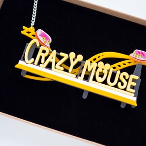 May include: A yellow and black necklace with a roller coaster design and the words "Crazy Mouse".