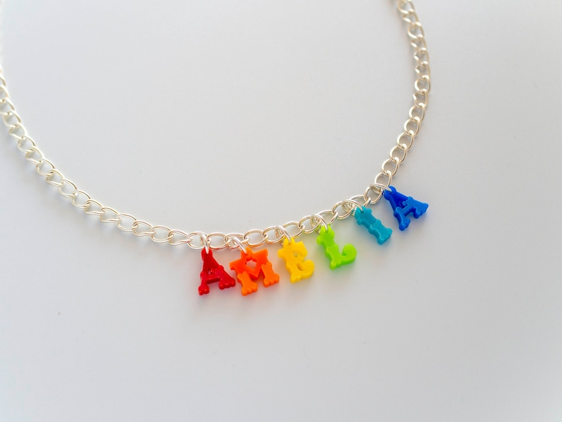 May include: A silver chain necklace with colourful plastic letters spelling out the name "AMELIA". The letters are in rainbow order, starting with red and ending with blue.