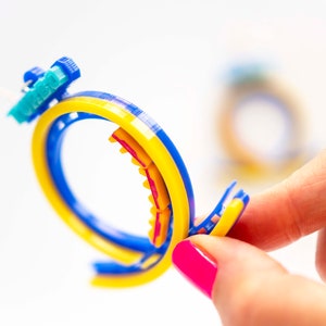 Pu&ograve; includere: Un anello di plastica colorato con accenti blu, gialli e rossi. L'anello &egrave; composto da pi&ugrave; strati di plastica e ha una superficie testurizzata.