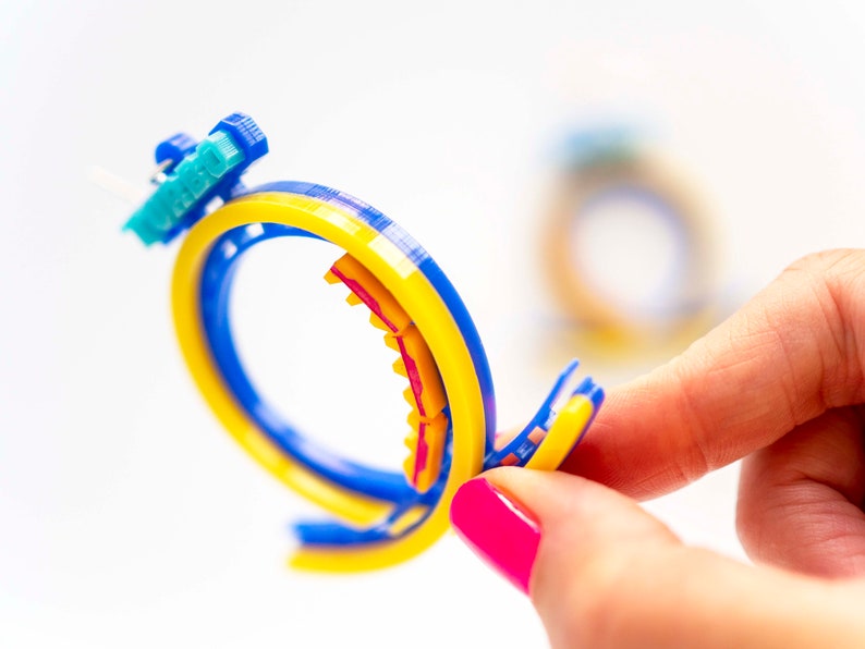 Pu&ograve; includere: Un anello di plastica colorato con accenti blu, gialli e rossi. L'anello &egrave; composto da pi&ugrave; strati di plastica e ha una superficie testurizzata.