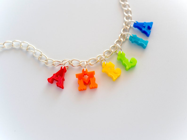 Puede incluir: Un collar de cadena de plata con abalorios de letras de colores que deletrean "FAMILY". Los abalorios son rojos, naranjas, amarillos, verdes, azules y morados.