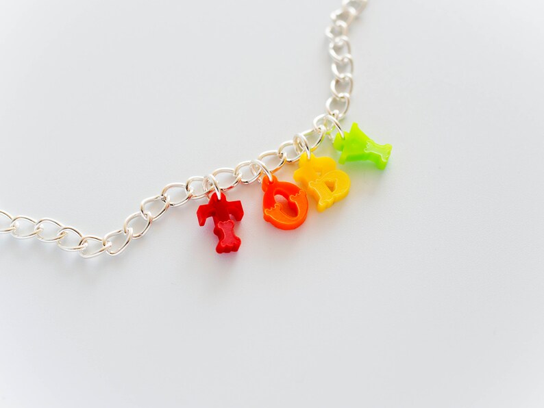 Puede incluir: Un collar de cadena plateada con abalorios de letras de colores que deletrean la palabra "TODAY". Los abalorios son rojos, naranjas, amarillos y verdes.