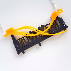 May include: A black and yellow necklace with a roller coaster design. The necklace features the words "Crazy Mouse" on the roller coaster.