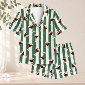 Op de afbeelding: Een pyjamaset met een pyjamashirt met korte mouwen en knoopsluiting en een bijpassende short, voorzien van een donkergroen en wit verticaal gestreept patroon met een herhalende print van bruine cocktailglazen en witte biezen.