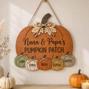 May include: A wooden pumpkin-shaped wall hanging with a jute rope hanger. The large pumpkin features the text Nana & Papa's PUMPKIN PATCH. Five smaller pumpkins are attached at the bottom, each labeled with the names Liam, Emma, Noah, Sophia, and Harper.