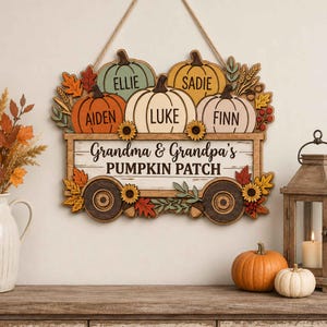 May include: A wooden wall hanging shaped like a wagon filled with pumpkins, featuring the text "Grandma & Grandpa's PUMPKIN PATCH" and the names "ELLIE", "SADIE", "AIDEN", "LUKE", and "FINN" printed on the pumpkins, decorated with autumn leaves.