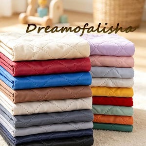 May include: A stack of folded quilted fabric pads in various solid colors including cream, red, blue, brown, gray, black, lavender, pink, yellow, orange, and green. Each pad features a diamond-shaped stitched pattern. The text Dreamofalisha is visible.