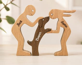 May include: A set of three stylised wooden figurines featuring two light-toned human figures and one dark-toned dog figure. The human figures are engraved with the names Jack and Sophia, while the dog figure is engraved with the name Cooper.