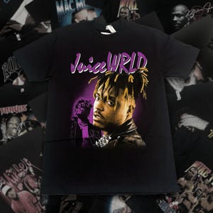 May include: A black short-sleeve t-shirt featuring a graphic print of the artist Juice WRLD. The design includes the text "Juice WRLD" in purple lettering above a portrait of the artist with dreadlocks, set against a purple and black background.