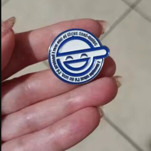 May include: A circular enamel pin featuring a blue and white laughing face logo with a horizontal bar across the center. The outer border contains the text, I thought what I'd do was, I'd pretend I was one of those deaf-mutes.