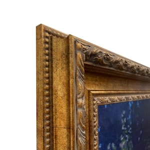 Pode incluir: Uma moldura retangular com acabamento em ouro metálico e uma superfície texturizada e ornamentada, apresentando uma borda externa com contas e um padrão de folhas esculpidas ao longo da borda interna, envolvendo uma pintura azul escura com toques de folhagem verde.