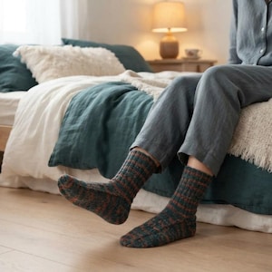 May include: A pair of mid-calf knit socks featuring a variegated pattern of dark green, charcoal, and rust orange tones. The socks are constructed with a ribbed texture throughout the leg and foot, providing a snug fit around the ankles and feet.