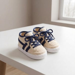 Può includere: Un paio di sneakers all'uncinetto color crema con strisce laterali blu navy scuro e lacci abbinati. Le scarpe presentano una suola in uncinetto bianco solido e una silhouette alta, realizzate con una lavorazione a maglia testurizzata.