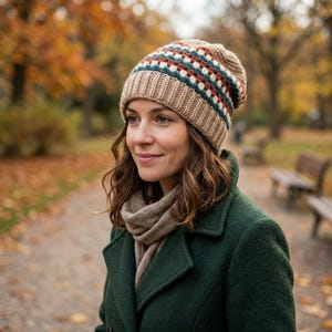 May include: A beige knit beanie featuring a ribbed brim and a decorative band of small, repeating squares in white, dark green, and rust orange. The hat has a textured, multi-colored pattern around the crown and a solid beige base.