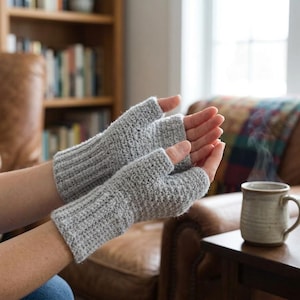 May include: A pair of light gray fingerless gloves featuring a textured knit pattern and a ribbed cuff design. The gloves cover the hand from the knuckles down to the wrist, leaving the fingers exposed for dexterity while providing warmth.