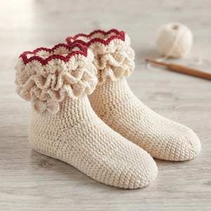 May include: A pair of cream-colored crochet socks featuring a ruffled cuff design with a dark red scalloped trim along the top edge. The socks are constructed with a dense, textured stitch pattern and include a small decorative bow on the side.