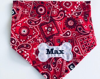 May include: Red bandana dog collar with a white bone-shaped patch embroidered with the name "Max" in black. The bandana features a paisley pattern in red, white, and navy blue.