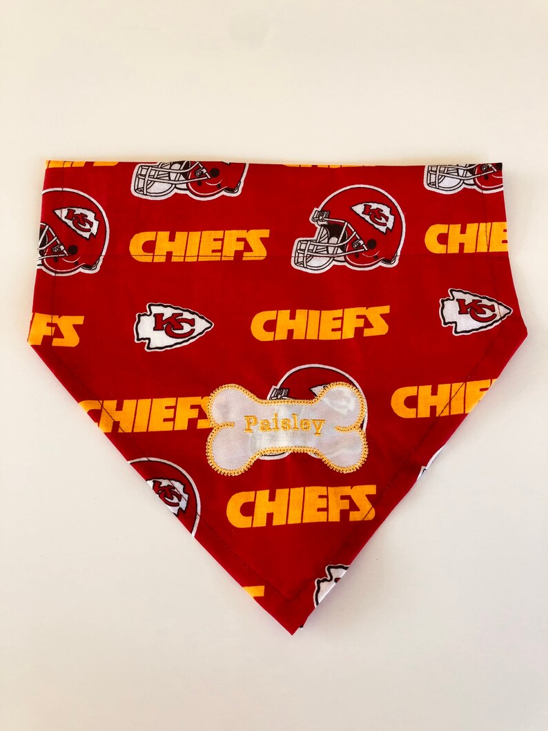 May include: Red and gold dog bandana with a white bone-shaped tag that says "Paisley" and a pattern of Kansas City Chiefs logos.