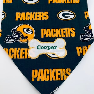 May include: Green and gold dog bandana with a bone-shaped patch that says "Cooper" and a repeated pattern of the Green Bay Packers logo.