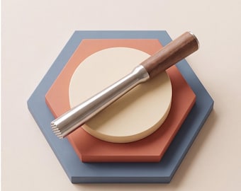 Puede incluir: Un mortero para cócteles con un mango de madera de color marrón oscuro liso y un cuerpo cilíndrico de acero inoxidable, que presenta una base texturizada y ranurada diseñada para triturar ingredientes con precisión.