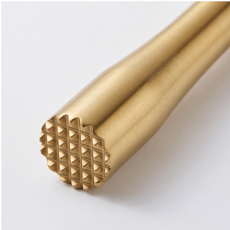 Puede incluir: Un mortero de c&oacute;ctel cil&iacute;ndrico con un acabado dorado cepillado. La base de la herramienta presenta un patr&oacute;n texturizado en forma de rejilla que consiste en peque&ntilde;as formas piramidales elevadas dise&ntilde;adas para triturar ingredientes.