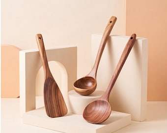 Puede incluir: Tres utensilios de cocina fabricados en madera marrón con vetas visibles. El conjunto incluye una espátula de borde plano y dos cucharas de cuenco redondo, cada una con un mango largo y un pequeño orificio circular en el extremo superior.