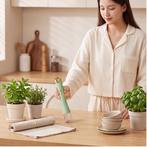 May include: A handheld light green electric kitchen tool with a gold-coloured top and a clear base, featuring a small logo on the side. The device has a cylindrical body and a whisk-like attachment at the bottom for mixing or blending ingredients.